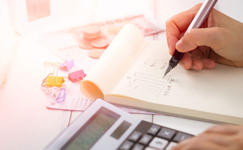 An image of an accountant's hands writing in a notebook and using a calculator